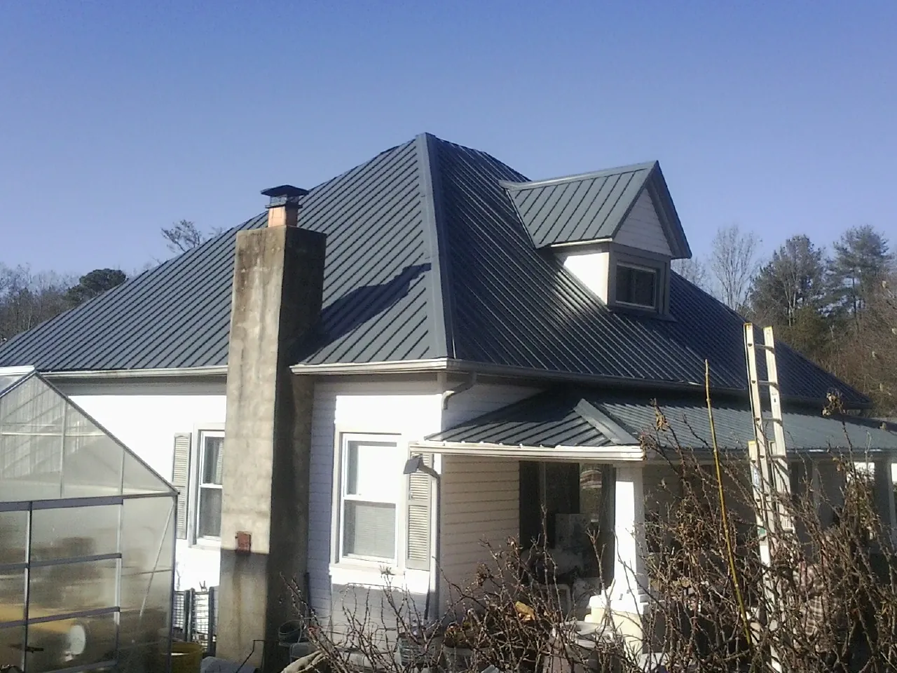 Dark blue standing seam metal roof on a white farmhouse with dormer — Slate & Tile Roof Repair by Roofing Brothers in Copperhill