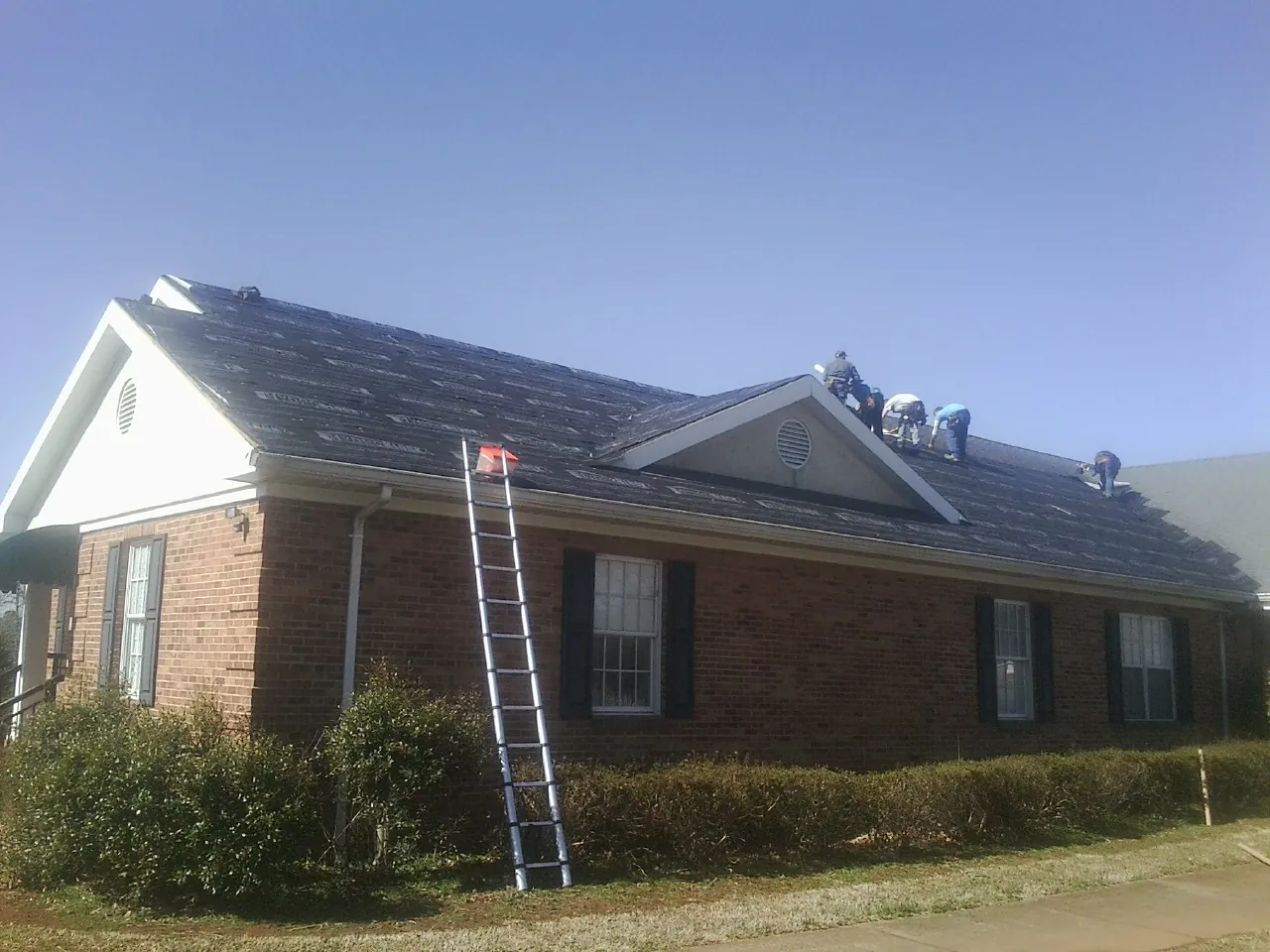 Crew tearing shingles off a brick ranch roof with a ladder set — Metal Roof Repair work by our crew in Copperhill