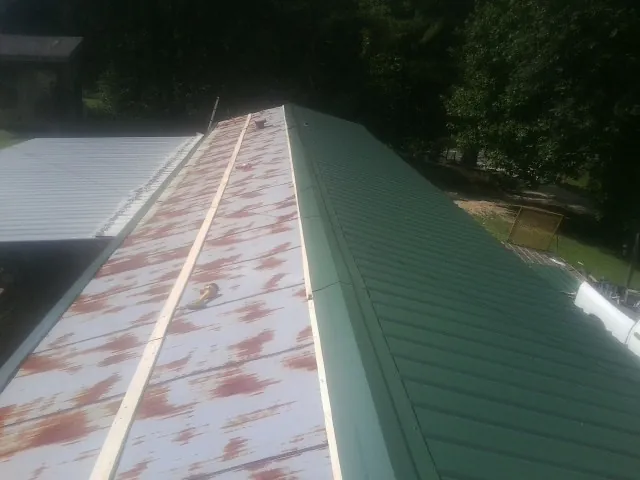 Old rusted panels beside newly installed green metal roofing — Wind Damage Roof Repair by Roofing Brothers in Copperhill
