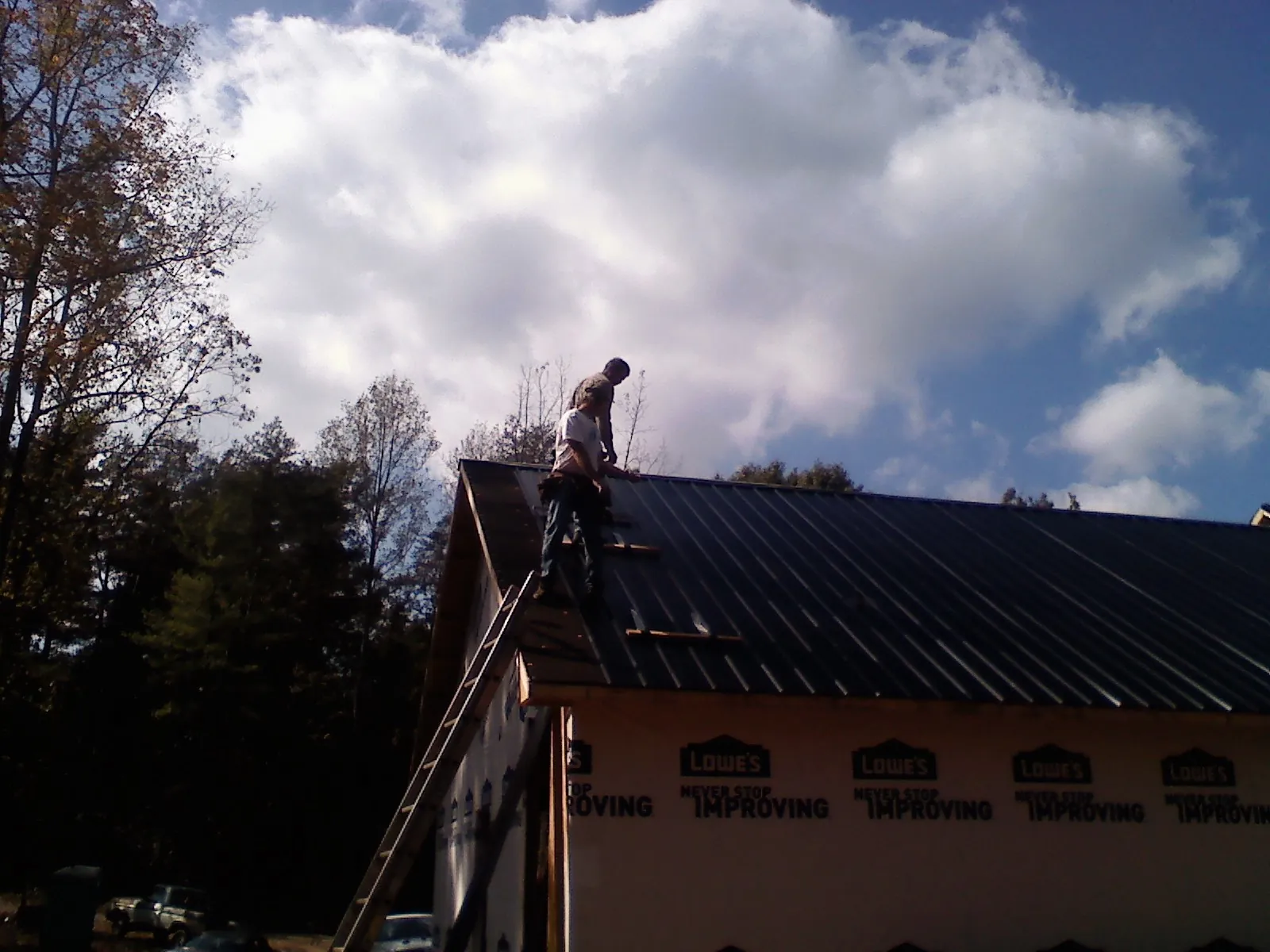 Roofer fastening dark metal panels high against a cloudy sky, from a Roof Inspection job in Copperhill