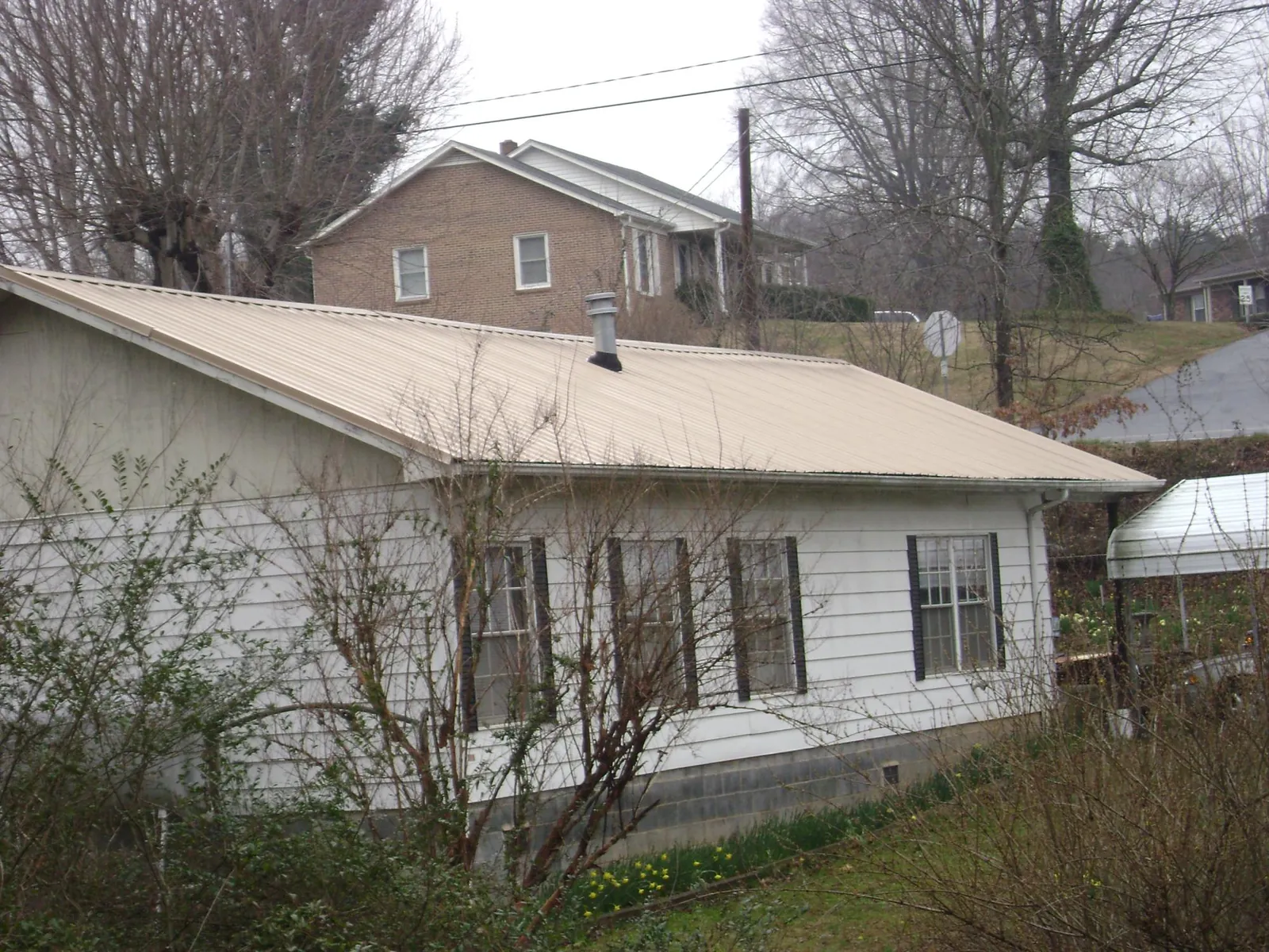 Tan metal roof on a white sided house set into a hillside — Commercial Roofing by Roofing Brothers in Copperhill